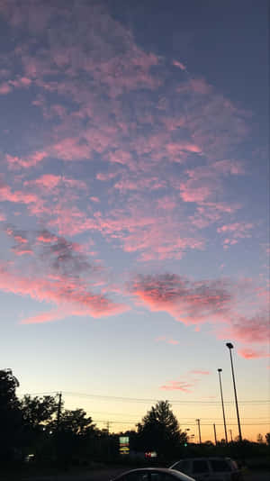 停車場上空粉紅和紫色的日落雲，下方是樹木和汽車的剪影。 — 雲朵 壁紙