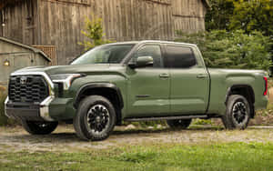 橄欖綠色的豐田Tundra皮卡車停在木製穀倉和草地附近。