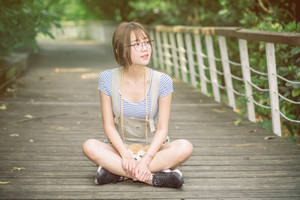 戴眼鏡的年輕女性盤腿坐在公園的木製步道上。