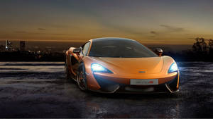橙色McLaren 570S跑車停在暮色中的濕漉漉路面上，背後有城市燈光。 — 汽車 壁紙