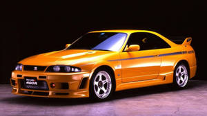攝影棚燈光下的橙色日產Skyline R34 Nismo 400R跑車。