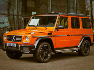 橙色 Mercedes G63 AMG SUV 停泊在玻璃建築外。 — 汽車 壁紙