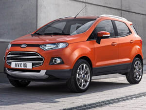 橙色福特EcoSport SUV停泊在混凝土牆附近的行人路上。
