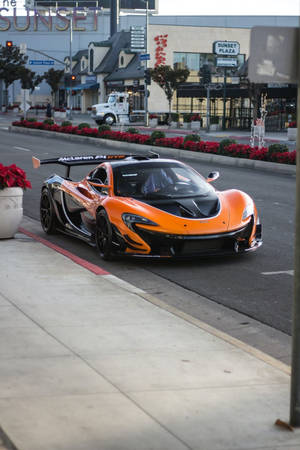 橙色McLaren P1 GTR停泊在城市行人路上，靠近紅色聖誕紅和Sunset Plaza標誌。
