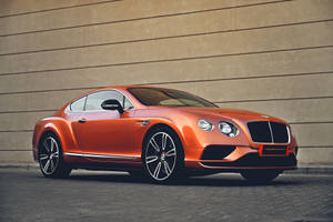 橙色 Bentley Continental GT 停泊在米色牆壁旁的行人路上。 — 汽車 壁紙