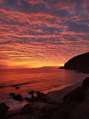 海洋上空戲劇性的夕陽，熾熱的紅色和橙色雲彩倒映在水中。