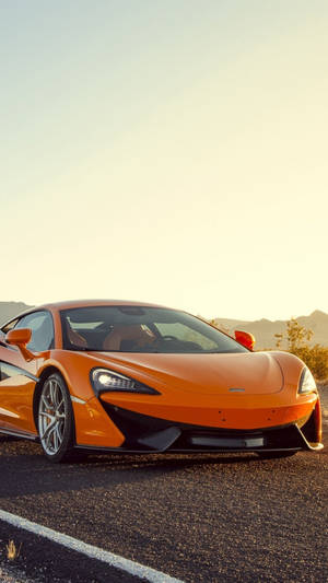 橙色McLaren跑車停在路上，有山脈和夕陽。 — 麥拿侖 GIF 壁紙