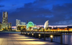 黃昏時分的城市海濱，燈火通明的建築物和摩天輪。 — 日落大道 壁紙