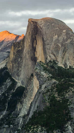 Half Dome 山被金色光芒照亮，下方森林，多雲天空