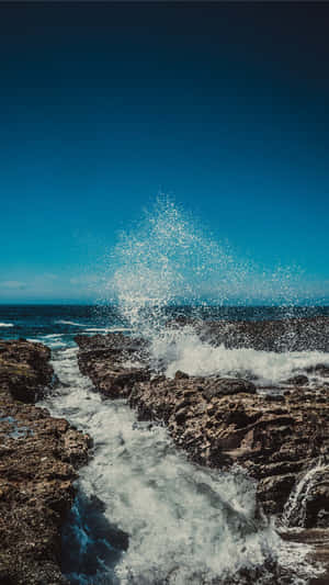海浪衝擊黑色岩石，白色水花飛濺，背景是藍天。