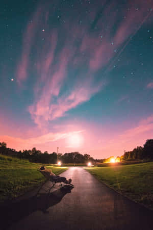 人坐喺小路嘅椅子上，喺星空下，有粉紅色同藍綠色嘅雲 — 淺粉紅色美學動圖 壁紙