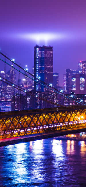 夜晚的布魯克林大橋，城市燈光在紫色天空下倒映在水面上。