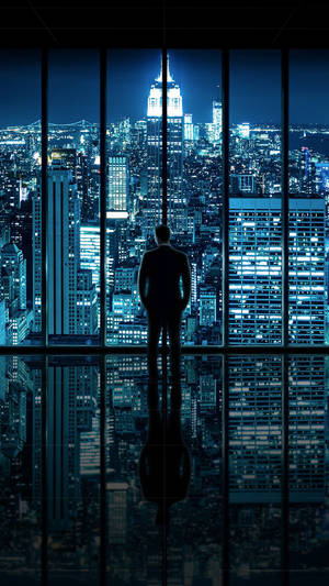 一個男人凝視窗外夜晚發光的城市景觀的剪影。 — 紐約市 壁紙