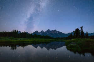 星空下，銀河系倒映在山峰和樹木下的湖中。 — 夜空 壁紙