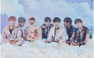 七位身穿花卉服裝的 K-pop 偶像面帶笑容坐在雲朵上。