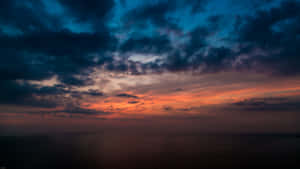 海洋上戲劇性的日落，火橙色雲彩映襯著深藍色的暮色天空。 — 日出 壁紙