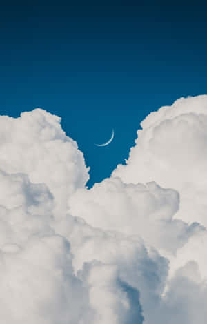 在深藍色天空中，蓬鬆的白雲之間可見一彎月牙。