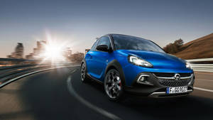 藍色Opel Adam Rocks在日落時分在蜿蜒的道路上行駛，背景是城市天際線。