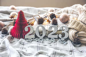 舒適的節日佈置，有2023數字、紅色樹、松果和針織品放在格仔毯上。