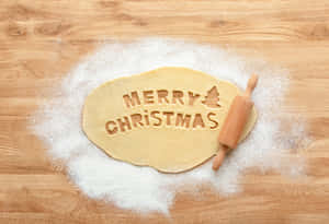麵糰上印有「Merry Christmas」和樹的圖案，在木桌上用麵粉呈現，旁邊有擀麵杖。