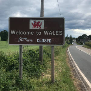 威爾斯邊境標誌，上面寫著「Welcome to WALES Sorry WE'RE CLOSED」，位於鄉村道路旁。