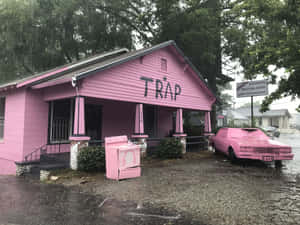 雨中的粉紅色建築物和汽車，側面有'TRAP'塗鴉。