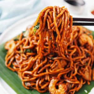 光澤的橙色麵條搭配蝦，用筷子夾起放在綠葉上。 — 美食 壁紙