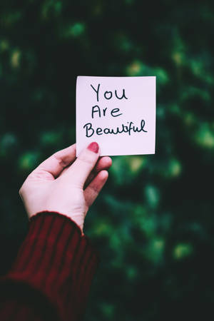 手拿著寫有 You Are Beautiful 的便條，背景為綠色