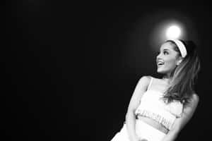 Ariana Grande 在聚光燈下穿著白色流蘇服裝在舞台上微笑。