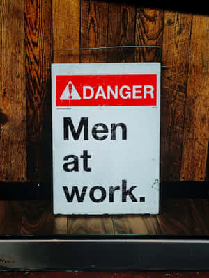 一塊磨損的警告標誌，上面寫著「Men at work」，安裝在木牆上。