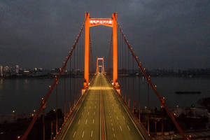 夜晚被照亮的橙色吊橋，空蕩的車道和遠處的城市燈光。 — 通往泰拉比提亞之橋 壁紙