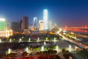 夜間城市景觀，有明亮的摩天大樓和一座發光的橋樑橫跨河流。 — 夜景城市 壁紙