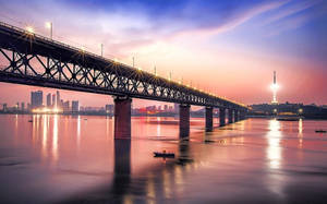 日落時分，一座發光的鋼橋橫跨河流，城市天際線和一艘小船。 — 通往泰拉比提亞之橋 壁紙