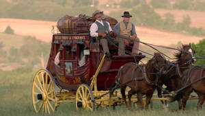 一輛紅色的 Wells Fargo 驛馬車，有兩名男子和兩匹馬在草地上移動。