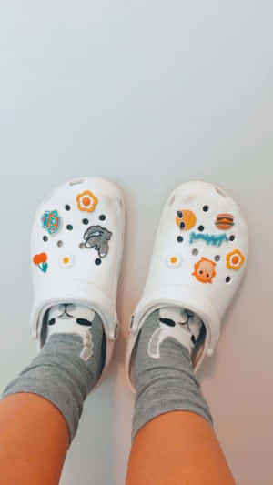 穿著白色Crocs鞋的腳，鞋上有卡通飾物和灰色貓咪襪子。
