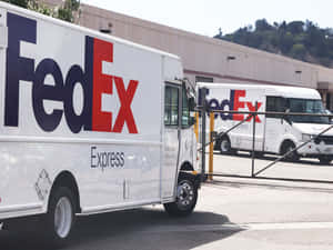 陽光明媚的日子裡，兩輛FedEx送貨車停在倉庫設施。