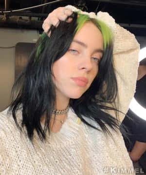 Billie Eilish 擁有綠色和黑色頭髮，身穿奶油色針織毛衣和銀色首飾。