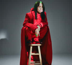 Billie Eilish 身穿紅色服裝在木凳上吹粉紅色泡泡糖泡泡。