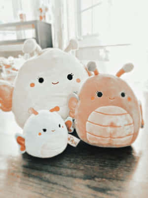 三個毛絨Squishmallows坐在靠近窗戶的木桌上。 — 美學 壁紙
