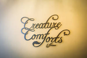 金屬牆藝，上面用優雅的草書寫著「Creature Comforts & Fierce」。