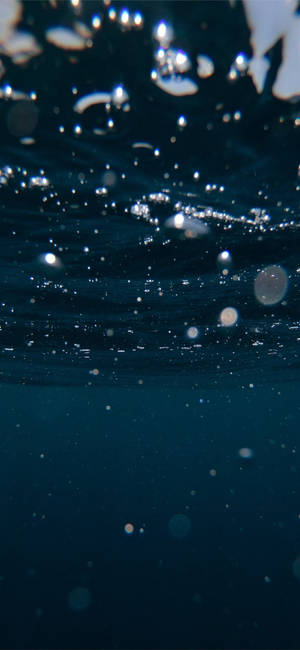 氣泡在深藍色海水中上升，帶有陽光反射。 — iPhone 14 Pro Max 壁紙