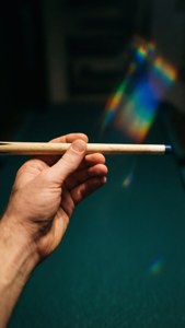 手握住桌球桿，在綠色絨布桌面上帶有彩虹光效