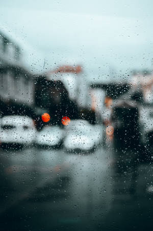 窗戶上的雨滴俯瞰著模糊的城市街道，帶有橙色車燈。