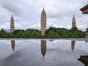 三座塔倒映在寧靜的池塘中，周圍環繞著綠樹和多雲的天空。 — 建築 壁紙