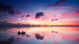 在色彩繽紛的日落天空下，平靜水面上小船裡的兩個人。 — 湖景 壁紙