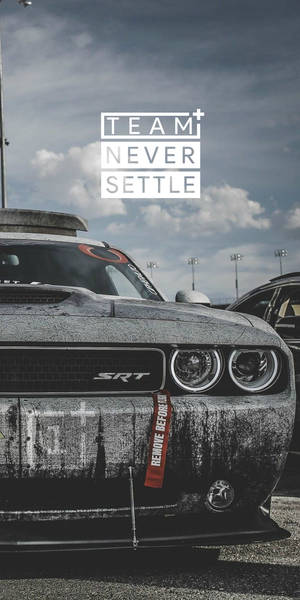 風化黑色道奇挑戰者SRT在賽車場上，帶有「TEAM NEVER SETTLE」字樣。