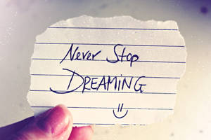 手拿著一張撕破的紙條，上面有訊息「Never Stop DREAMING」和一個笑臉。