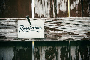 手寫便條釘在風化木柵欄上，寫著Resolutions。