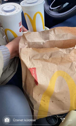 麥當勞飲品和紙袋在車內，有一隻手拿著一個杯子。 — Galaxy Tab A11 壁紙