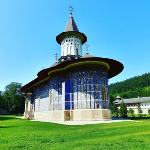 一座藍色東正教教堂，帶有宗教壁畫，位於靠近山脈的綠色草坪上。